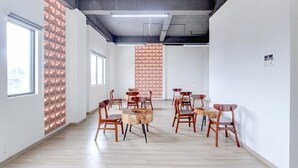 Ruime kamer met houten vloer, meerdere stoelen, een ronde centrale tafel en een behang met patroon.