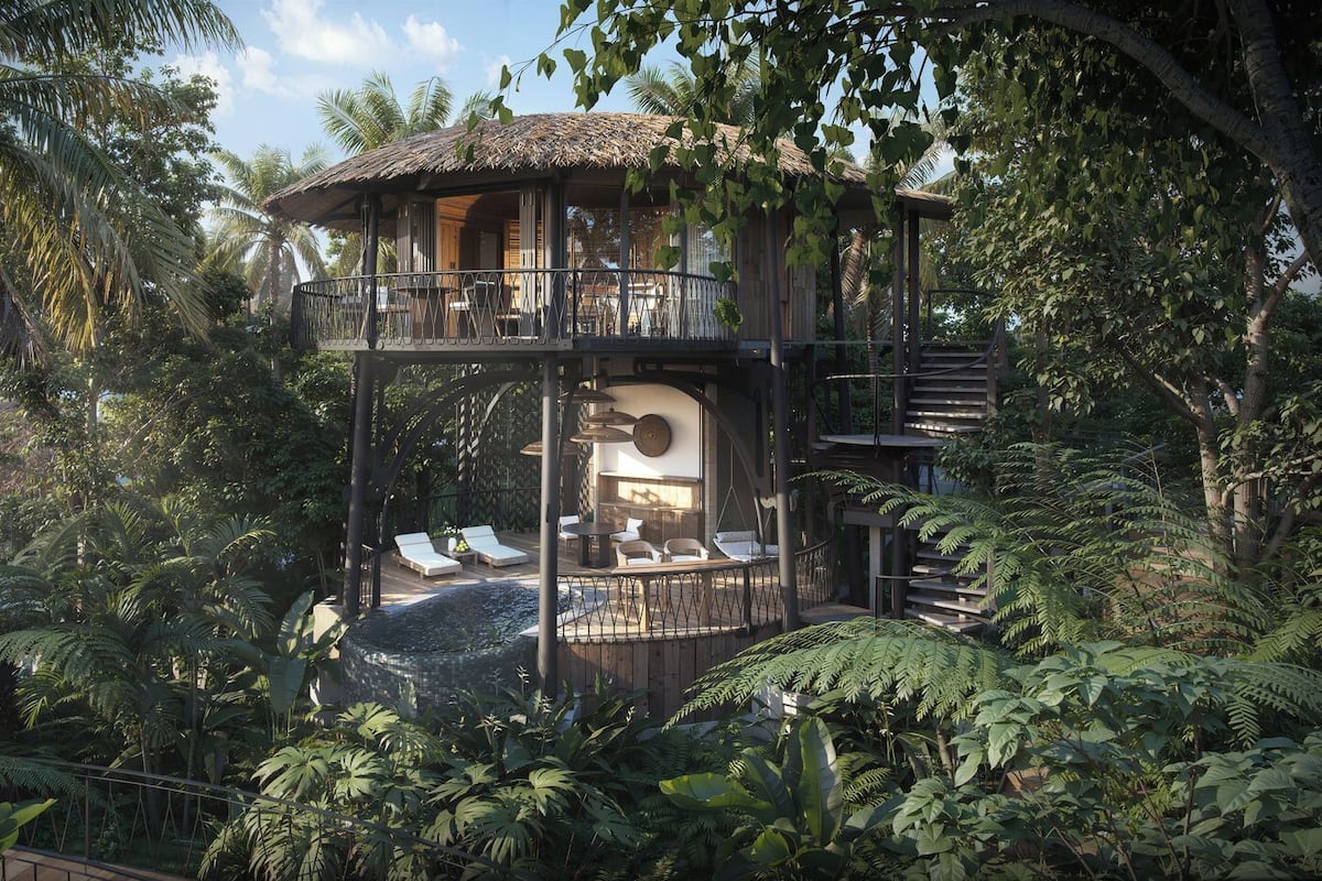 A multi-level wooden structure with a thatched roof, surrounded by lush tropical vegetation.