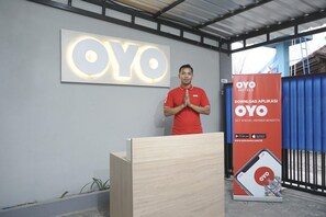 Une personne se tient devant un pupitre, et un grand logo OYO est visible sur le mur derrière elle.
