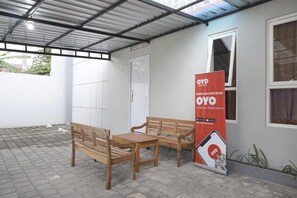 Un espace extérieur abrité, doté d’un banc et d’une table en bois, d’une porte blanche et d’une banderole publicitaire pour les hôtels OYO.