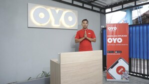 Una persona de pie frente a un atril, con un gran logotipo de OYO en la pared de fondo.