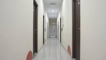 Un long couloir étroit, avec des portes de chaque côté, un sol carrelé et un plafond doté d’un éclairage encastré.