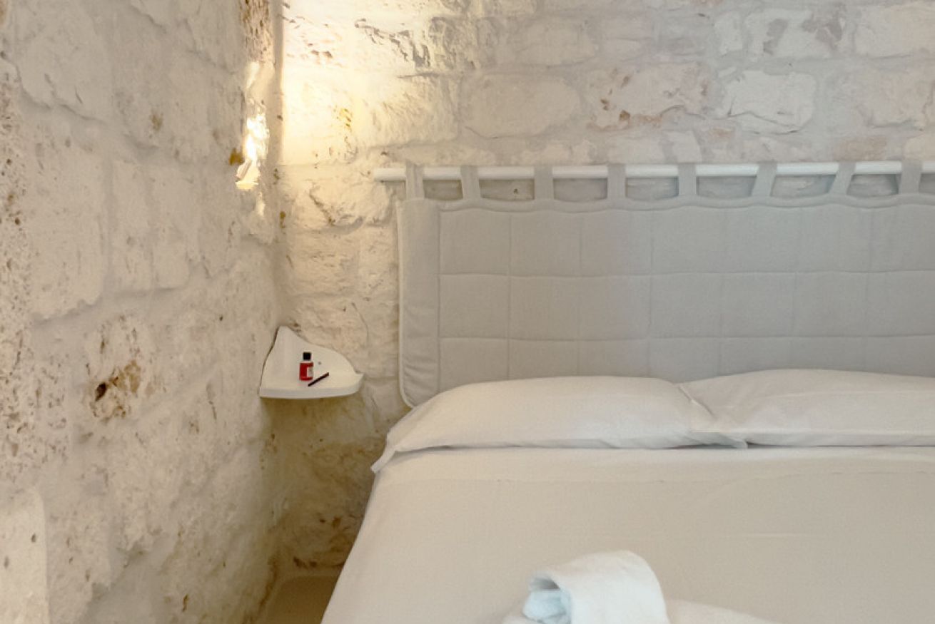 Ein Zimmer mit weißer Ziegelwand, einem weißen Kopfteil und einem Nachttisch mit Lampe.