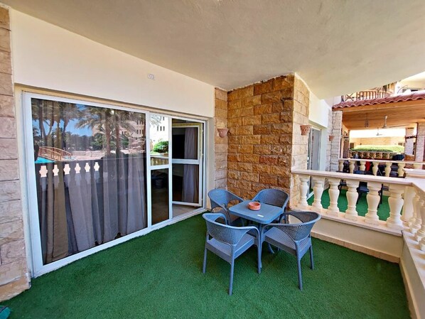 A balcony with a table and chairs, a stone wall, and a view of a building through a glass door.