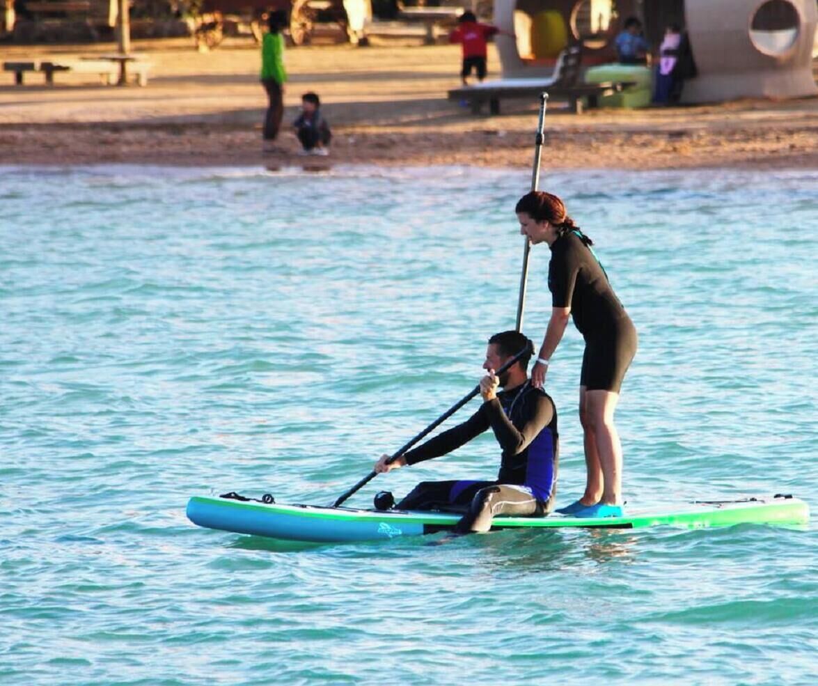En person på et paddleboard i vandet, mens en anden person står i nærheden.
