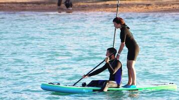 En person på et paddleboard i vandet, mens en anden person står i nærheden.