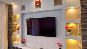 A modern living room with a large flat-screen TV mounted on a wall, surrounded by built-in shelves with decorative items. - Palma Suites Hurghada (Hurghada)