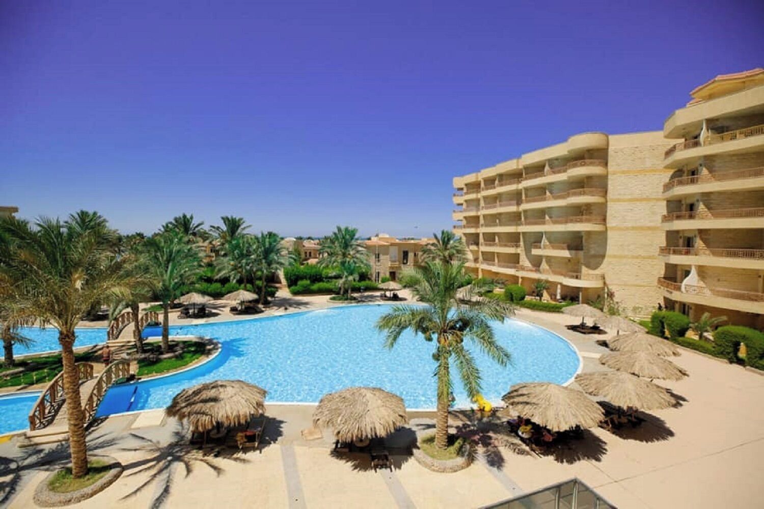 Ein Resort mit großem Pool, Palmen und einem mehrstöckigen Gebäude.