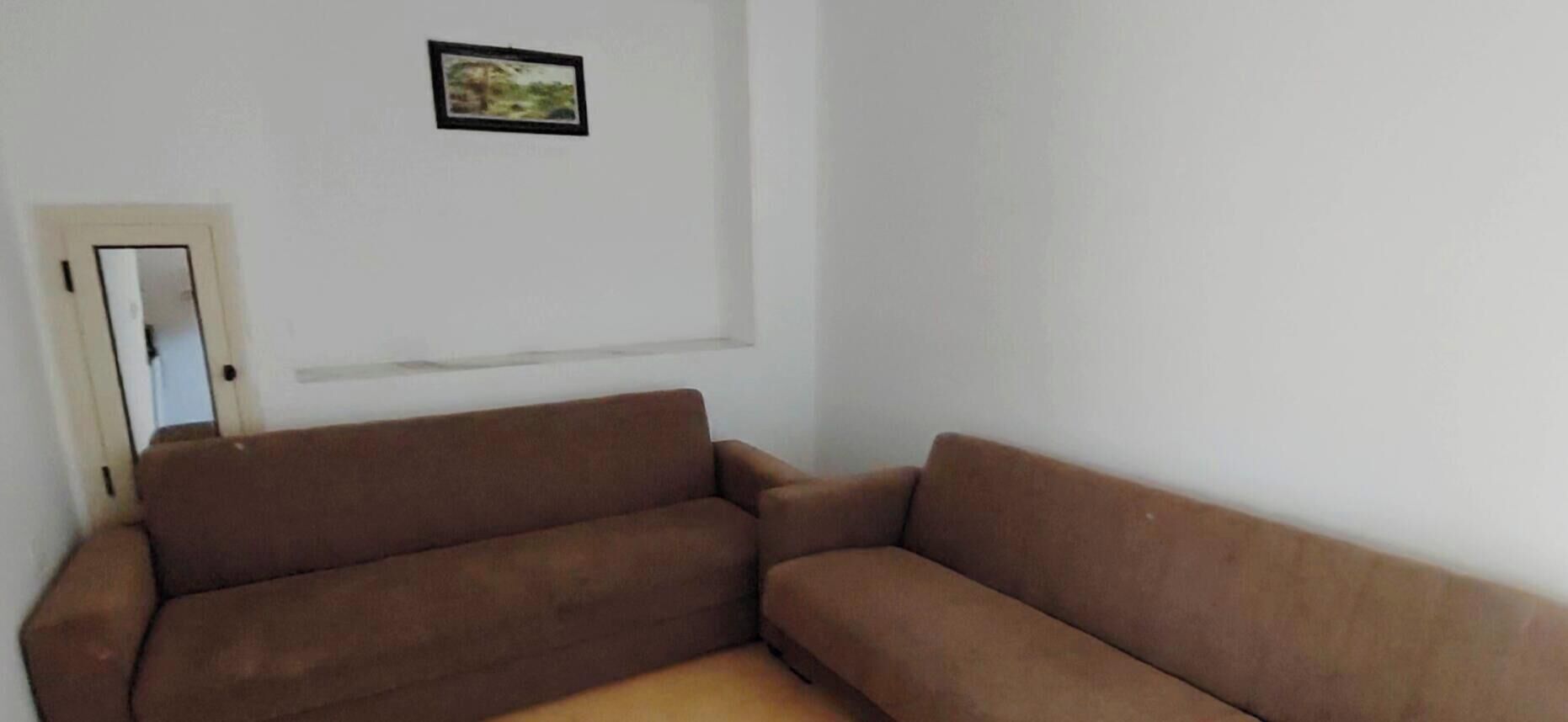 A room with a brown sofa, a door, and a framed picture on the wall.