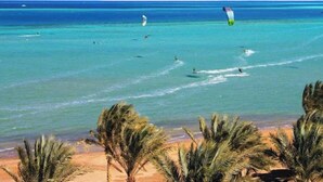 A beach with clear turquoise water, palm trees, and several kites in the sky. - Palma Suites Hurghada (Hurghada)