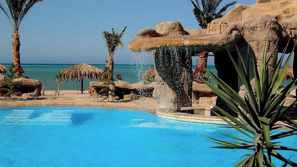 A pool with a waterfall feature, surrounded by rocks and palm trees. - Palma Suites Hurghada (Hurghada)