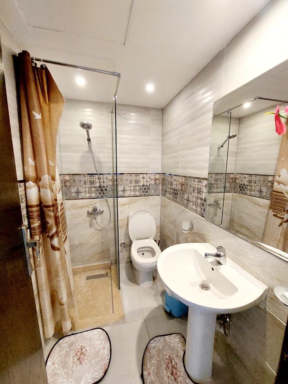Un baño con ducha, inodoro y lavamanos, que cuenta con un salpicadero de azulejos y un espejo grande.