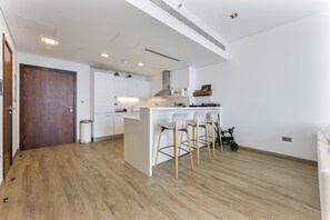 A modern kitchen with white cabinets, a wooden door, and a bar area with stools. - Chic 1BR APT in DIFC I 7-Min Drive to Burj Khalifa (Dubai)