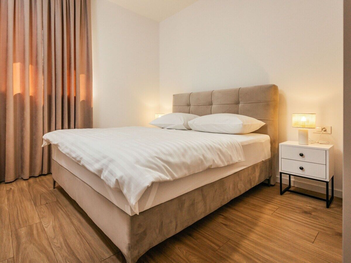A bedroom with a bed, nightstand, lamp, and curtains.