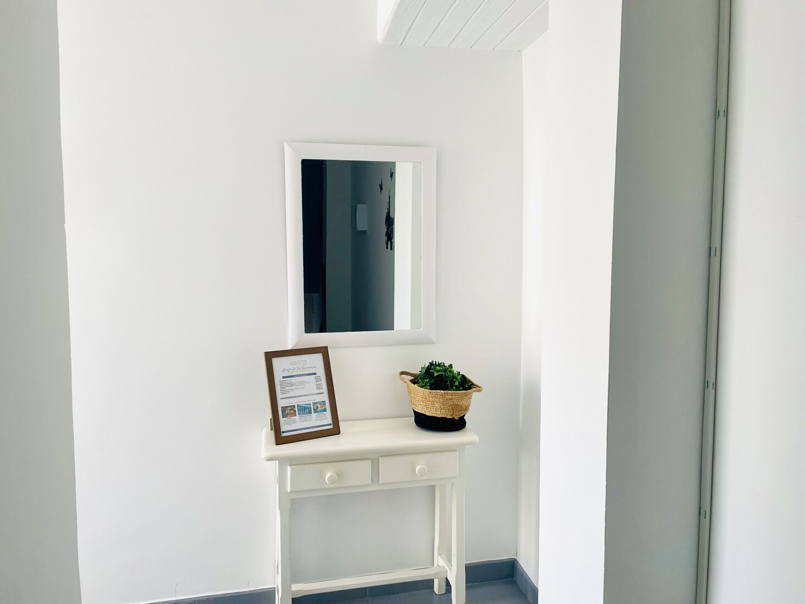 A white console table with a framed certificate, a small potted plant, and a window above.