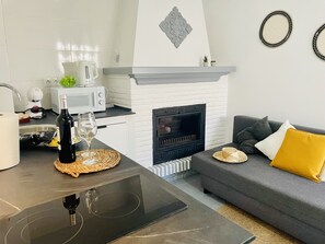 Una cocina moderna con microondas, tostadora y hervidor, una mesa de comedor con una botella de vino y una copa, una chimenea y un sofá gris con cojines amarillos.