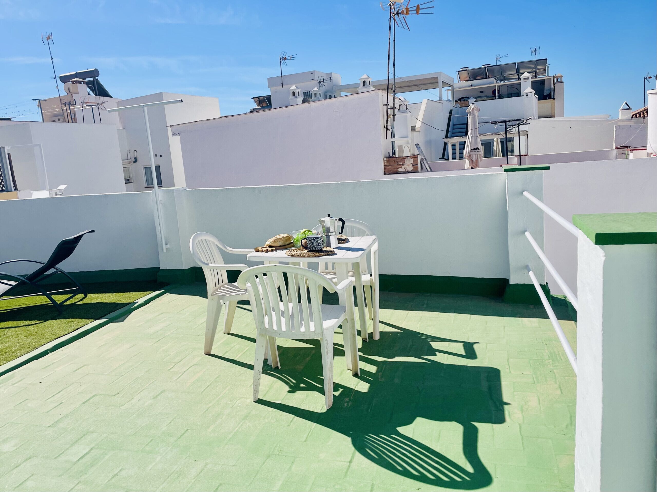 A rooftop terrace with a table, chairs, and a small garden area.