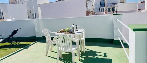 A rooftop terrace with a table, chairs, and a small garden area.