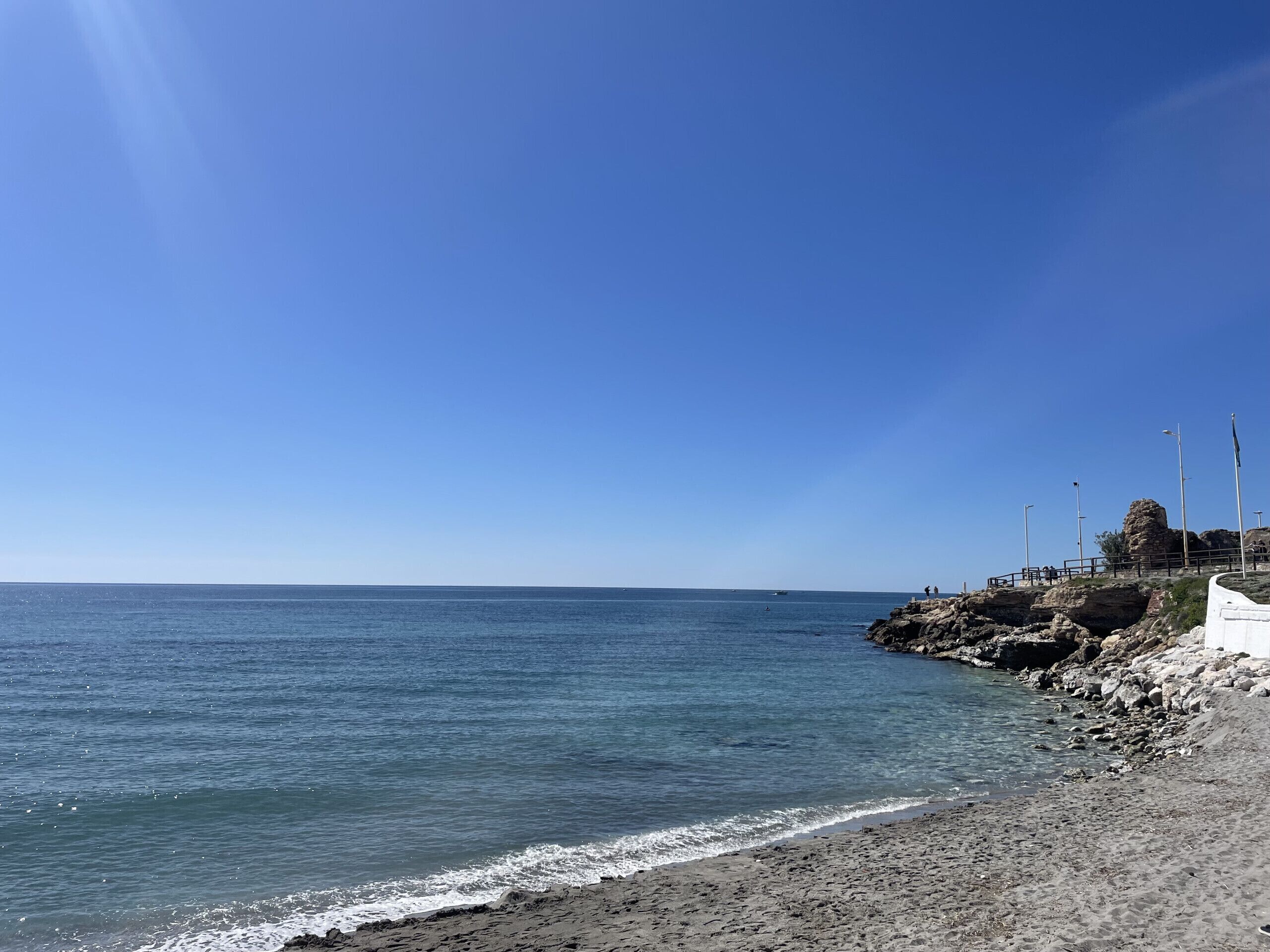 Una platja amb cel blau, aigua tranquil·la i terreny rocos.