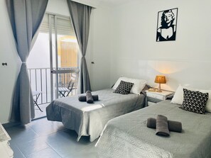 Quarto de hotel com duas camas, varanda, mesa e cadeira.
