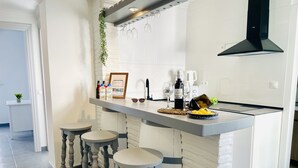 Een moderne keuken met een centraal eiland, barkrukken, een hangende lamp en een zwarte afzuigkap.