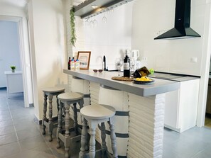 A modern kitchen with a central island, bar stools, a hanging light fixture, and a black range hood. - Caribbean Apartment by At Home Costa del Sol (Nerja)