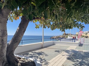 A coastal promenade with a clear view of the sea, a white building with a tiled floor, and a tree providing shade. - Caribbean Apartment by At Home Costa del Sol (Nerja)