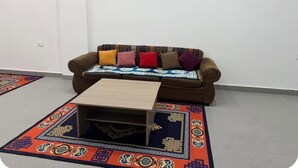 A brown sofa with colorful cushions, a wooden coffee table, and a patterned rug in a room with white walls.