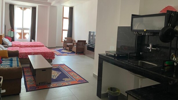 A modern living room with a sofa, a small table, a TV, and a kitchen area with a sink and stove.