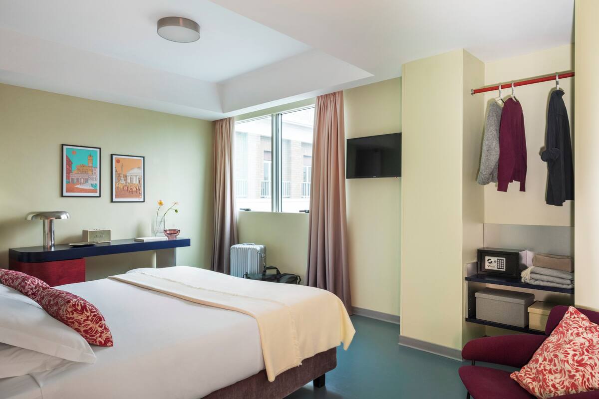 A hotel room with a bed, a desk, a TV, a wardrobe, and a window.