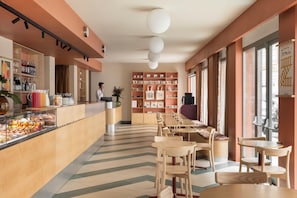 A modern cafe with a long counter, wooden chairs, and a variety of food items displayed.