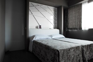 A modern hotel room with a bed, a headboard with a geometric pattern, and a window with curtains. - Moderno Hotel Roma (Rome)