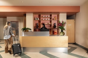 A reception desk with a receptionist, a plant, and a vase with flowers.