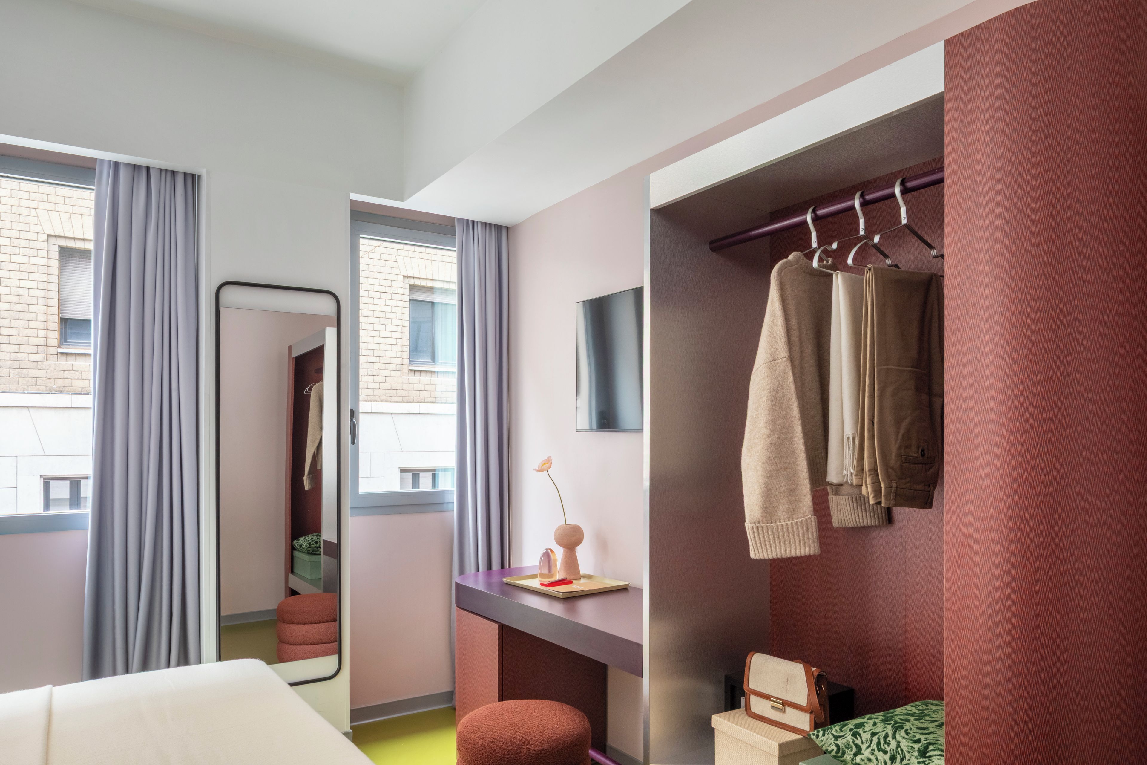 Habitación de hotel con cama, escritorio, espejo, toallero y vistas al exterior.