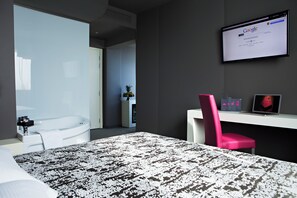 A modern hotel room with a bed, a desk with a computer, a pink chair, and a large screen displaying Google. - Moderno Hotel Roma (Rome)