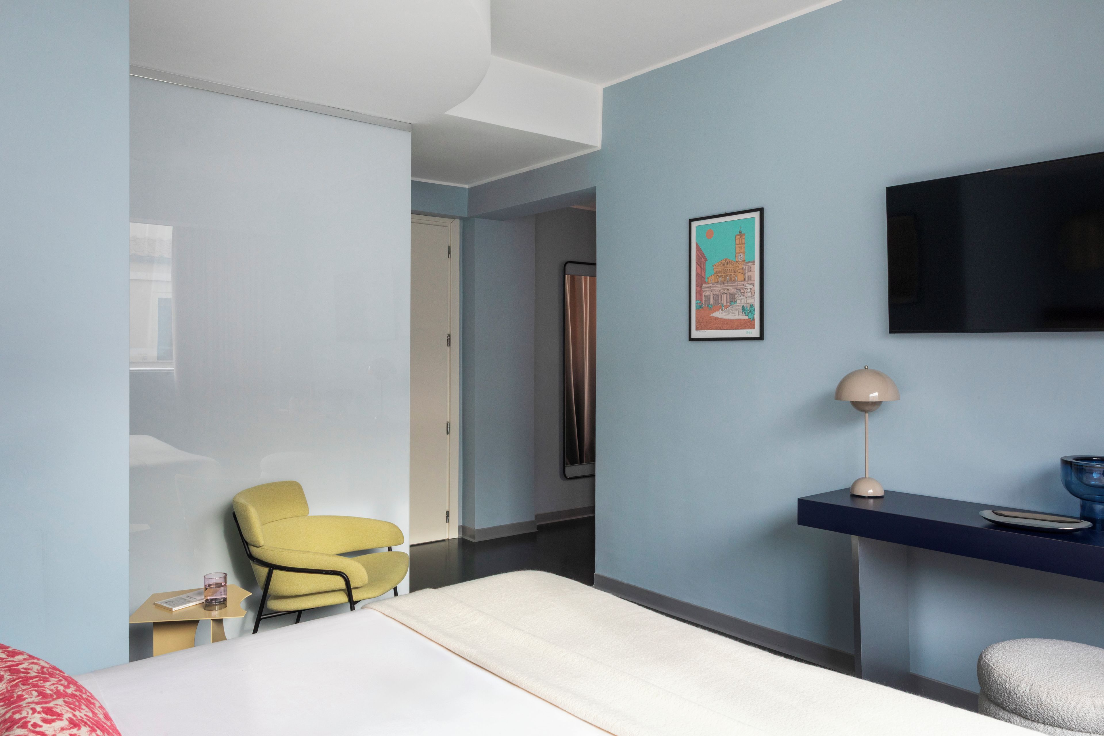 A modern hotel room with a bed, a desk, a chair, a TV, and a framed picture on the wall.