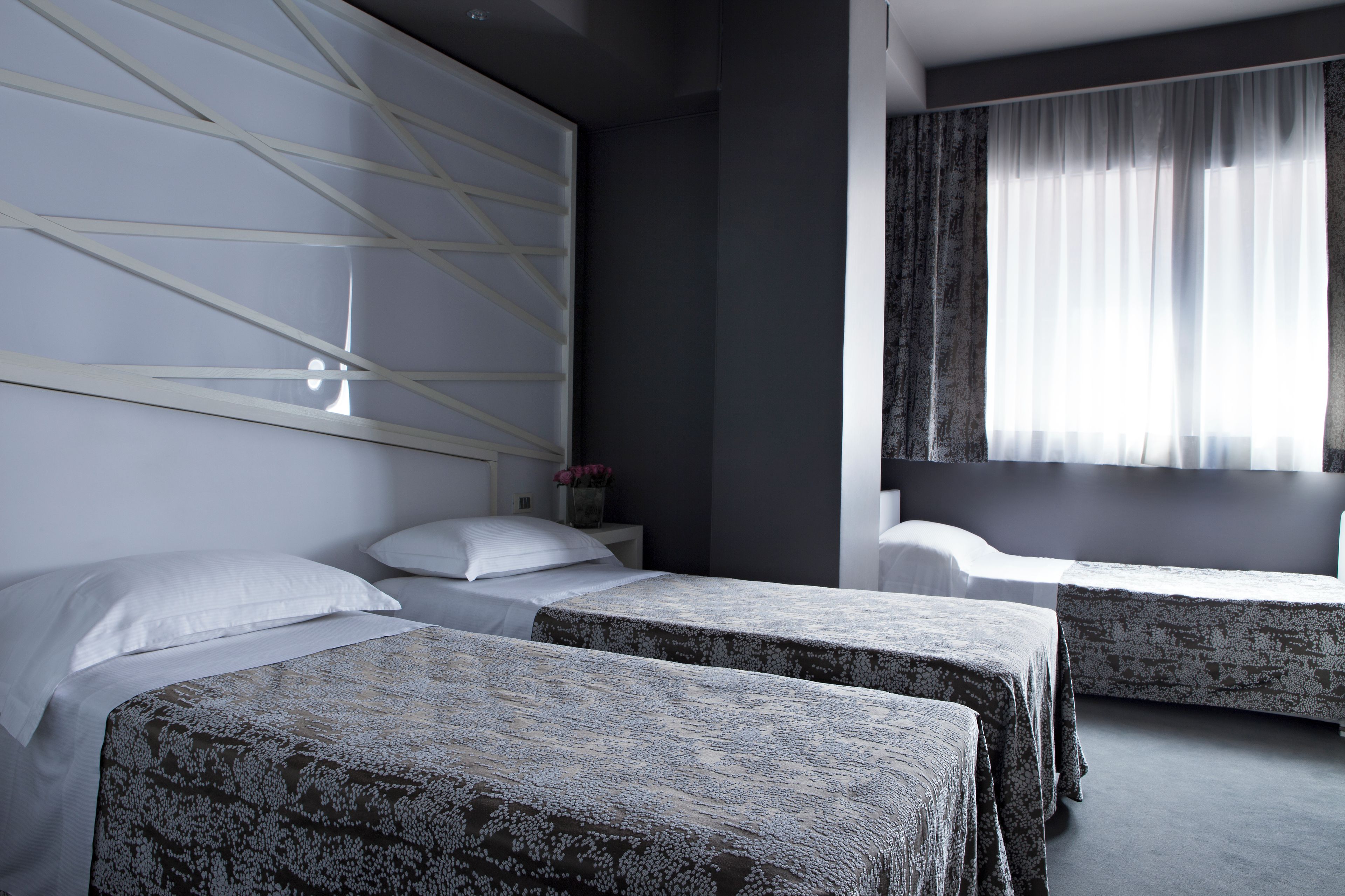 A hotel room with two beds, a large window with curtains, and a wall with a geometric design.