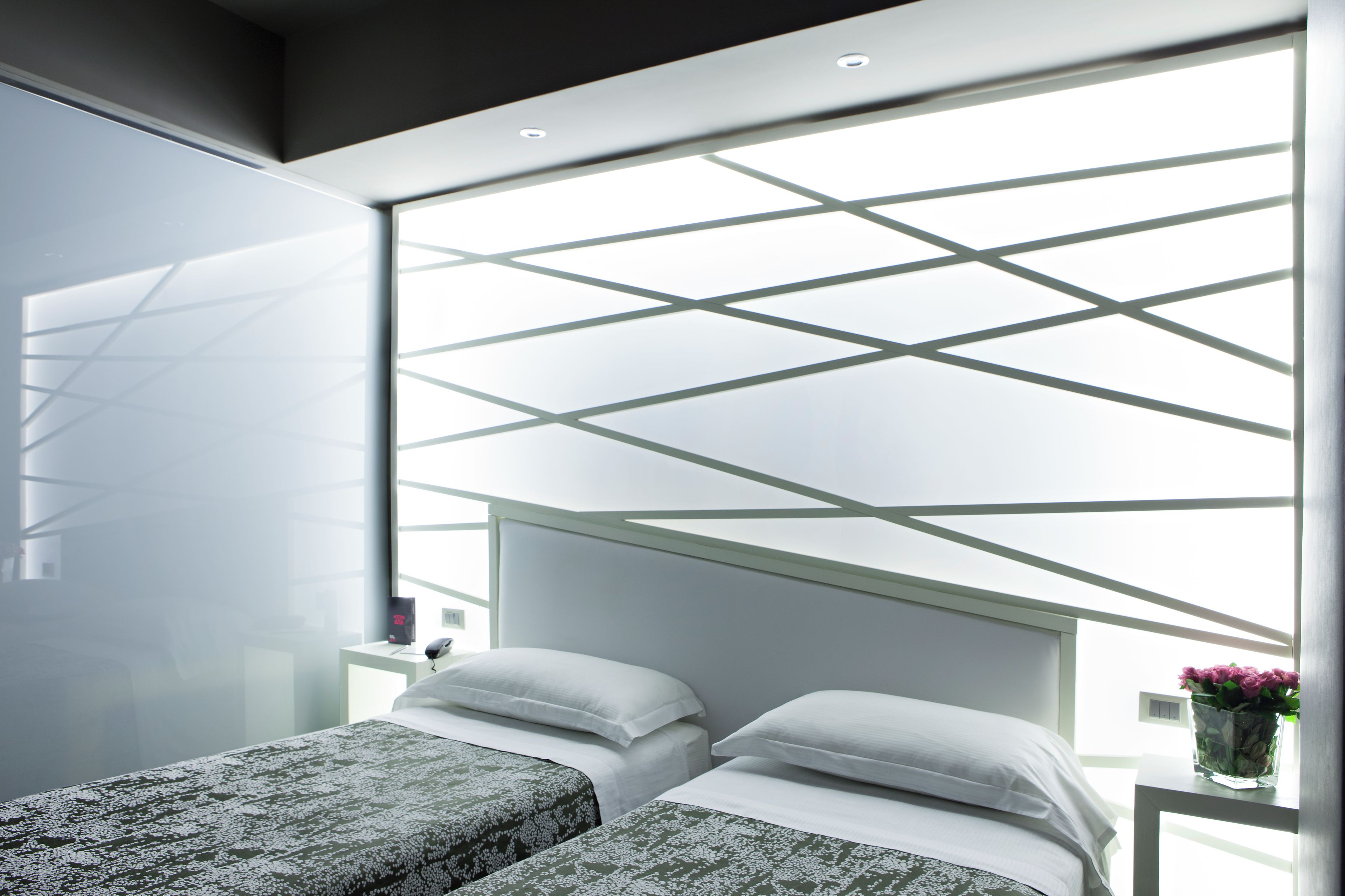 Een moderne slaapkamer met twee bedden, dakraam en nachtkastje met vaas.