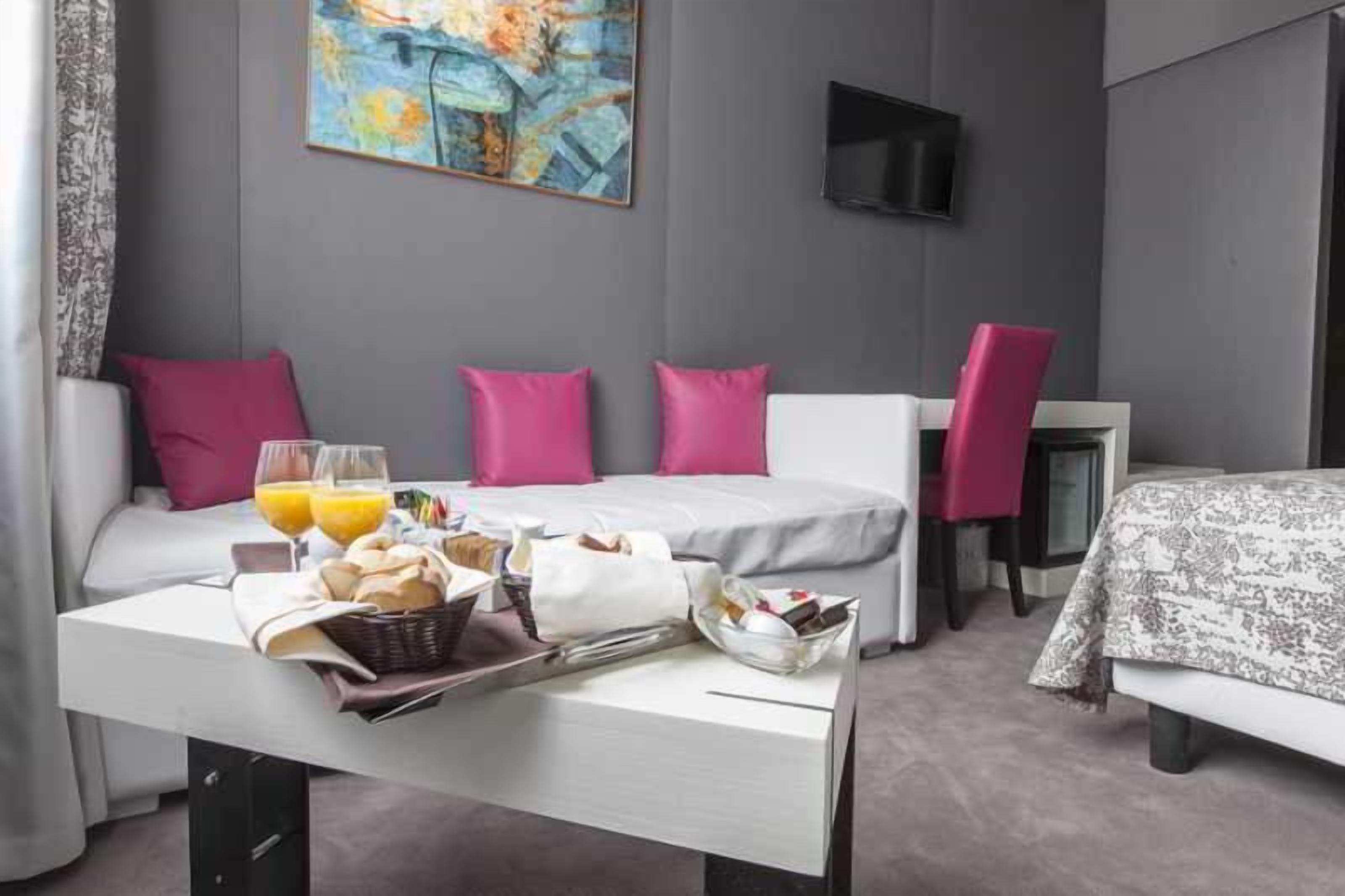 A hotel room with a bed, a table with breakfast, a TV, and a painting on the wall.