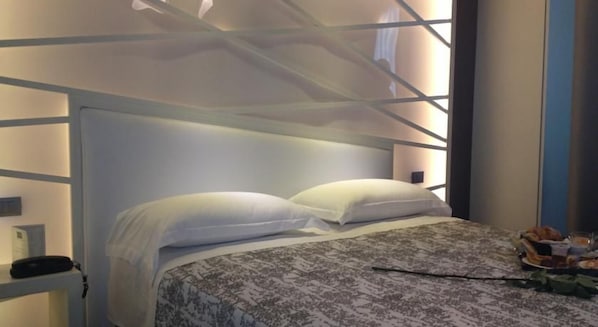 A neatly made bed with a patterned bedspread and two pillows, a bedside table with a lamp, and a window with a view of the outside. - Moderno Hotel Roma (Rome)