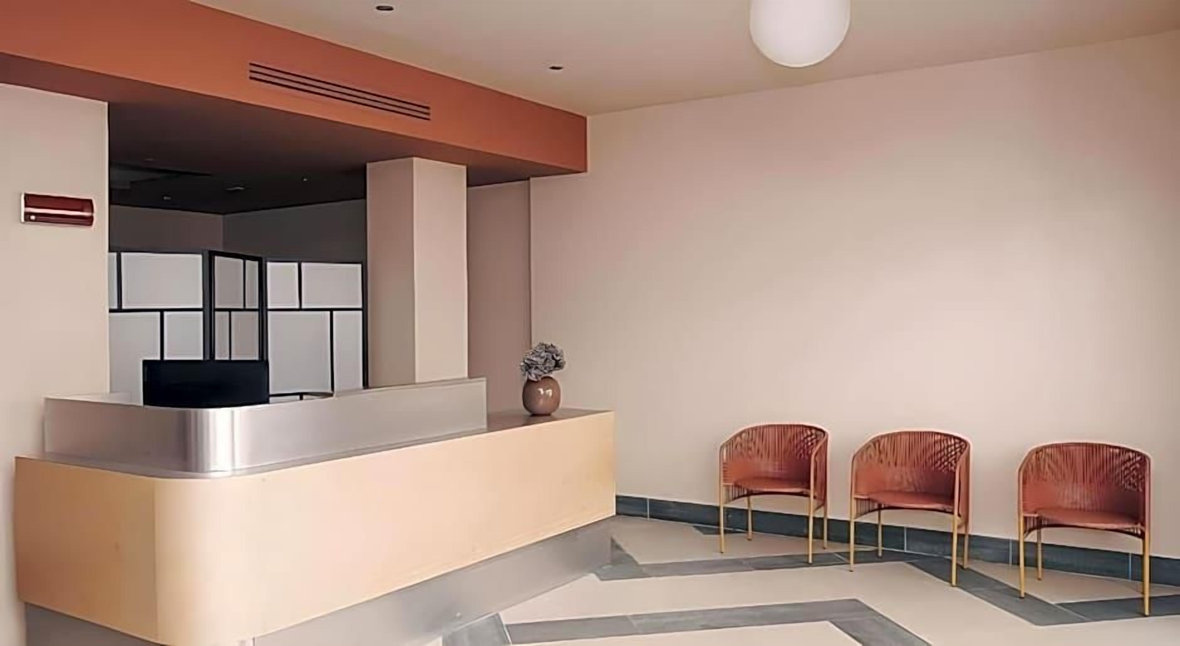 A reception area with a counter, three chairs, a vase, and a modern ceiling design.