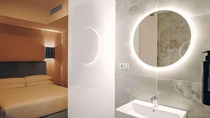 A modern bedroom with a bed, a bedside lamp, and a bathroom with a sink and mirror. - Moderno Hotel Roma (Rome)