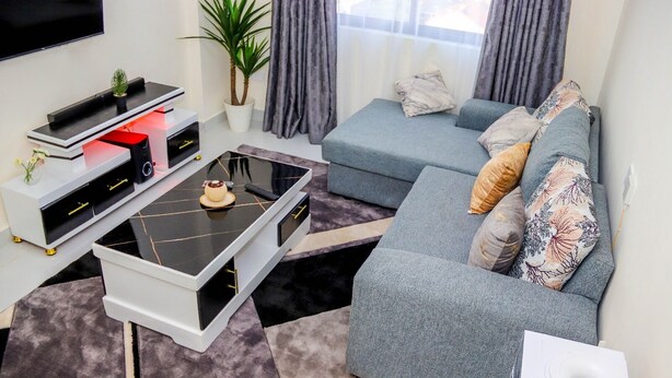 Ein modernes Wohnzimmer mit Flachbildfernseher, Couchtisch, Sofa und einem Blumentopf.
