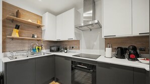 A modern kitchen with grey cabinets, a stainless steel range hood, a built-in oven, and a coffee machine. - Peaceful 1 bed apt in the Heart of Fitzrovia (London)