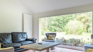 En stue med en sort lædersofa, et træbord og to lænestole med mønstrede hynder.