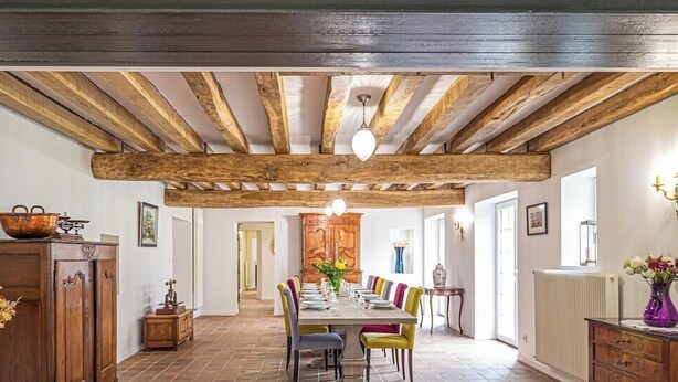 Et spiseområde med træloft, et langt bord og farverige stole.