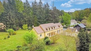 Et stort hus med velplejet græsplæne, omgivet af tæt skov.