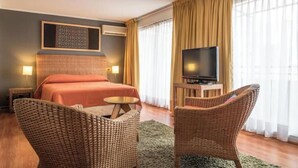 Ein Hotelzimmer mit Bett, Fernseher, Korbstühlen und einem großen Fenster mit Vorhängen.