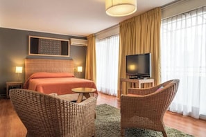 Ein Hotelzimmer mit Bett, Fernseher, Korbstühlen und einem großen Fenster mit Vorhängen.