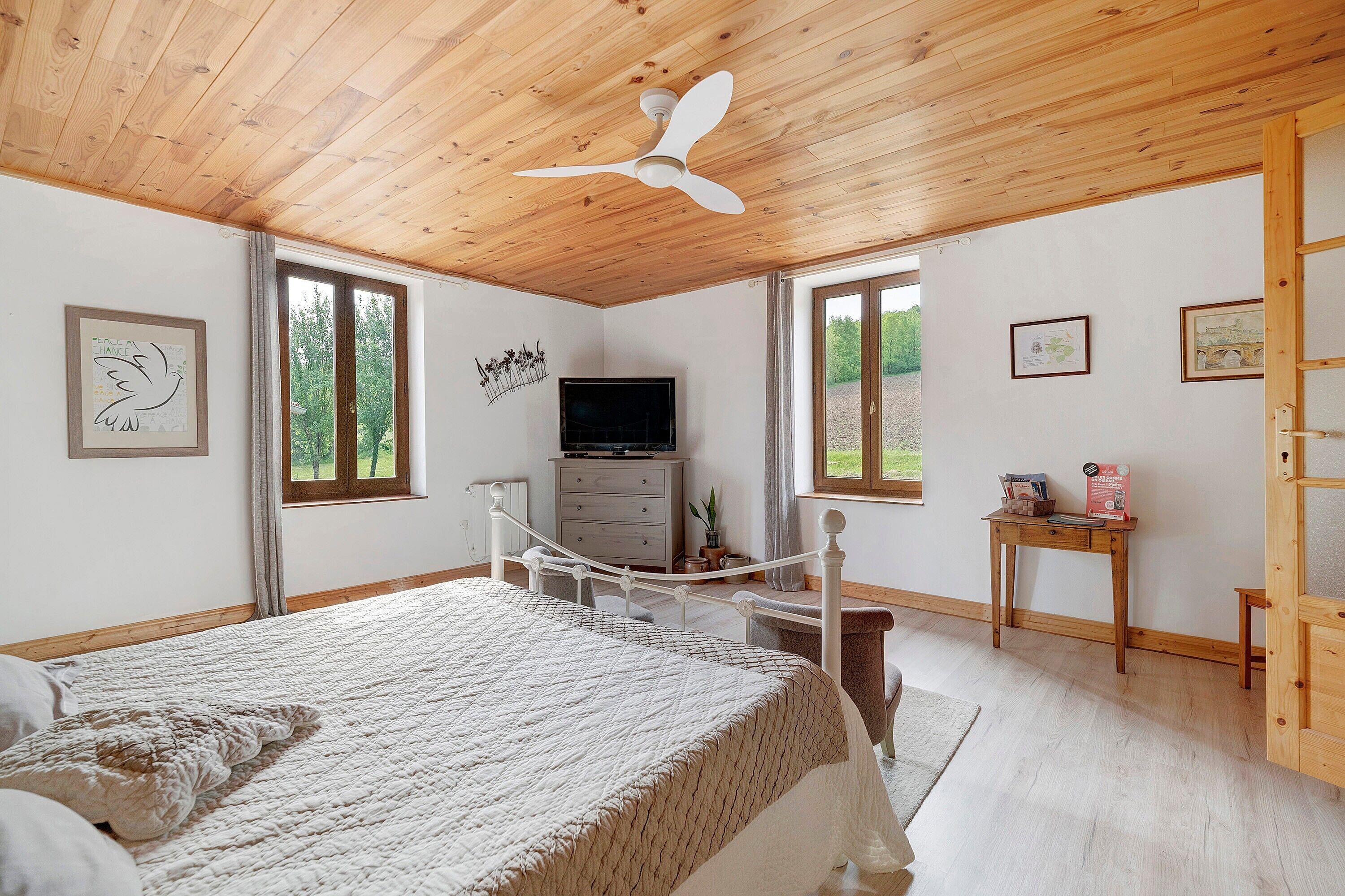 A bedroom with a bed, a ceiling fan, a TV, a dresser, and a window.